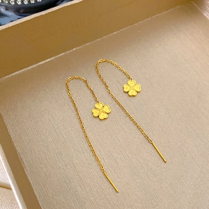 Dettaglio macro di orecchini a catena con quadrifoglio d'oro su vassoio testurizzato