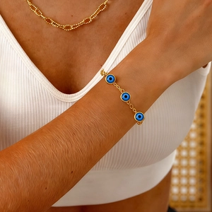 Bracelet chaîne dorée bohème avec trois perles d'œil bleu sur le poignet d'un modèle