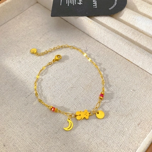 Close-up of gold chain bracelet with moon, bear pendants and red beads on display