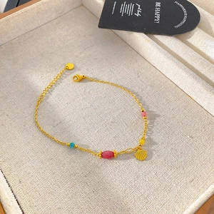 Detail view of a gold titanium bracelet featuring colorful beads and a shell charm