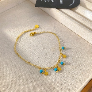 Detail of gold chain bracelet with star charms and turquoise beads on fabric display