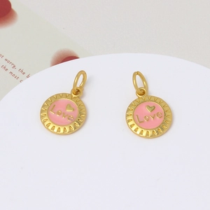 Macro shot of two round gold-plated charms with pink enamel Love heart centers