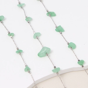 Detalle de piedras de cristal verde irregulares y cuentas plateadas en una cadena DIY