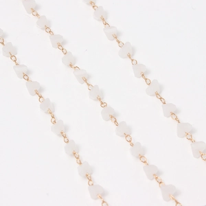 Detalle de cadena dorada con cuentas de corazón blanco translúcido para joyería artesana