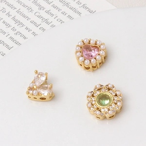 Macro detail of hollowed gold heart and floral pendants with pearls and zircons