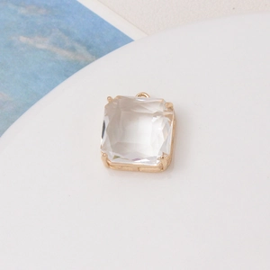 Close-up of a faceted transparent square glass charm with a gold-plated metal frame