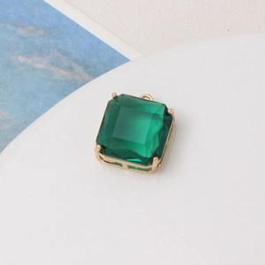 Detailed view of emerald-cut green crystal charm with gold-tone four-prong setting