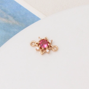 Close-up of a gold sunburst charm with a magenta center stone and dual connector rings