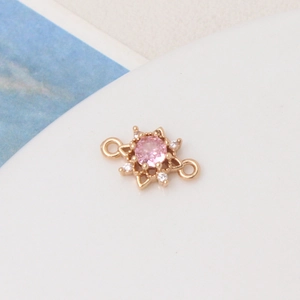 Macro view of gold sun charm with pink gemstone and zircon micro-paving on white surface