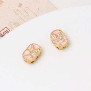 Detalle macro de cuentas ovales de metal dorado con esmalte floral rosa y agujeros