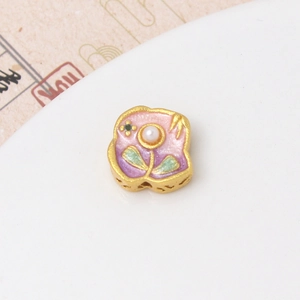 Primer plano de dije floral dorado con esmalte rosa y detalle de perla central