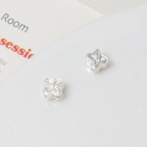 Macro shot of silver floral spacer beads with four petals and cross-etched flower centers