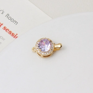 Macro view of gold-plated round clasp featuring a purple zircon and white crystal accents