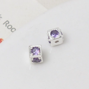 Macro detail of cube-shaped silver charms with purple cubic zirconia stones for DIY jewelry