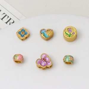Macro view of six gold-plated enamel beads with floral and butterfly patterns for DIY jewelry