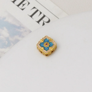 Macro view of gold flower bead with pink and blue enamel and red gemstone inlay