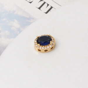 Detalle macro de cuenta ovalada chapada en oro con piedra azul tipo zafiro y circonita