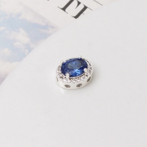 Detalle de cuenta ovalada de plata con gema azul y engaste de circonitas blancas