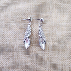 Détail de boucles d'oreilles argentées avec strass torsadés et cristal goutte d'eau