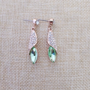 Détail macro de boucles d'oreilles or rose avec cristaux blancs et pierres vertes en forme de feuille