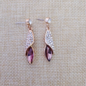 Détail macro de boucles d'oreilles feuilles d'or rose avec cristal marquise violet