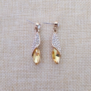 Gros plan de boucles d'oreilles dorées en gouttes avec pierres jaunes sur lin beige