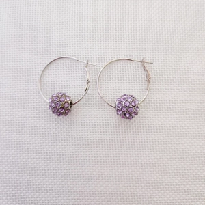 Dettaglio di orecchini a cerchio in argento con sfere di cristalli viola pavé su tessuto