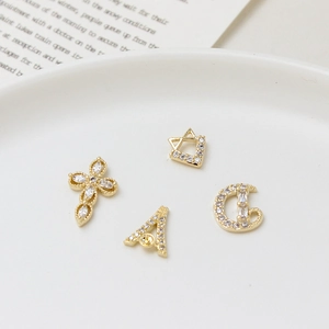 Golden micro-pave zircon nail art charms with cross and letter motifs in white tray