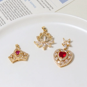 Tre eleganti pendenti a corona e cuore placcati in oro con cristalli rossi e zirconi su piatto