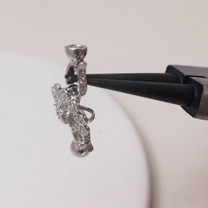 Detailopname van zilveren navelpiercing met witte strass steentjes vastgehouden door tang