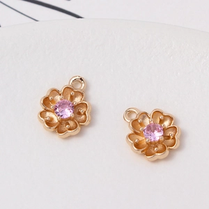 Close-up of golden floral pendants with pink zircon centers for DIY jewelry making