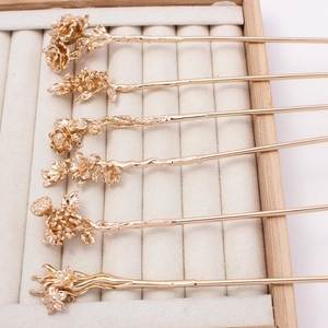 Detailed view of six champagne gold floral hairpins with intricate carvings on a velvet tray