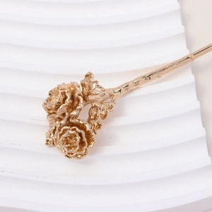 Macro shot of detailed golden metal flower hair pin on a white textured background