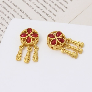 Detalle de pendientes de atrapasueños dorados con piedras rojas y plumas metálicas