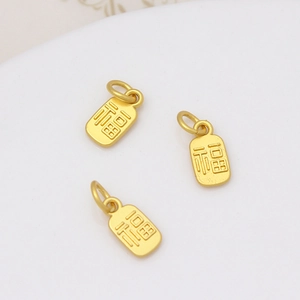 Détail macro de trois breloques dorées mates avec caractère Fu pour bijoux DIY