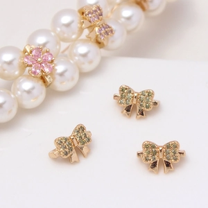 Detail of micro-set zircon flower and bow charms on a pearl bracelet gold spacer