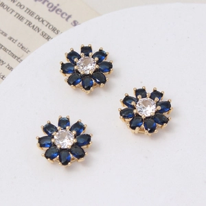 Macro detail of three daisy flower charms with blue stones and gold-plated setting