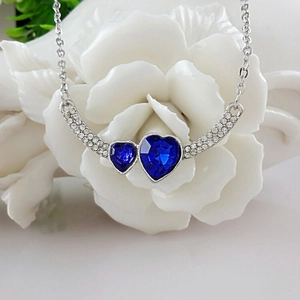 Elegante collana con pendente a doppio cuore blu e cristalli su una base a fiore bianco