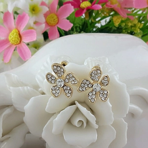 Orecchini a fiore dorati con strass scintillanti esposti su ceramica bianca decorativa