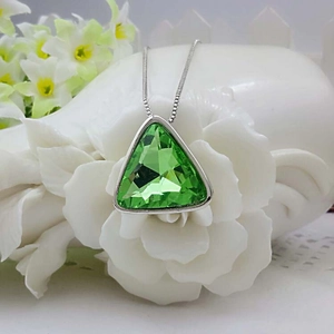 Close-up of a triangle green crystal pendant necklace displayed on a white ceramic flower