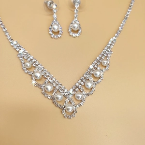 Close-up of bridal jewelry set featuring V-shaped pearl necklace and rhinestone earrings