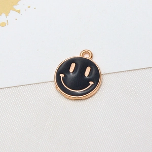 Macro detail of a black enamel smiley face pendant with gold plating for DIY jewelry
