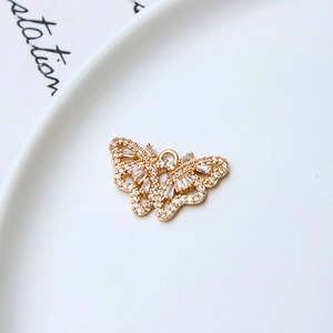Detailed view of a gold butterfly charm with micro-paved zircons on a white ceramic plate