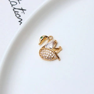 Macro detail of gold-plated swan pendant with white crystals and green eye stone