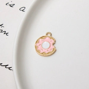 Detailopname van roze emaille donut-bedeltje met gouden metalen rand op wit porseleinen bord
