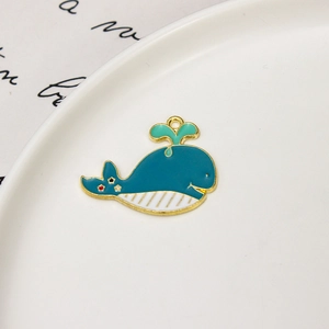 Detail shot of a blue whale-shaped alloy charm with green water drops and gold plating
