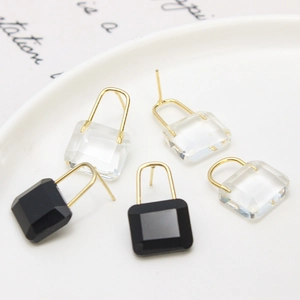 Boucles d'oreilles cadenas avec cristaux carrés clairs et noirs sur une assiette blanche