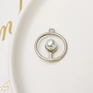 Close-up of a silver round pearl pendant on a white ceramic tray with gold decor