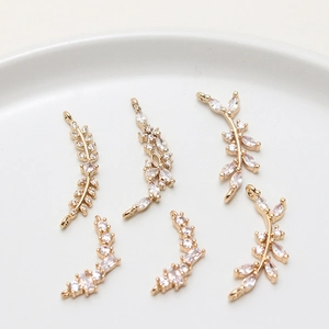 Detailed macro shot of gold-plated leaf pendants with zircons on a white ceramic tray