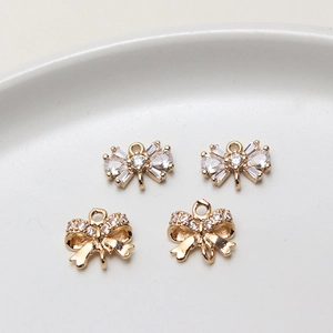 Détail de breloques nœuds dorés sertis de zircons étincelants sur une coupelle blanche